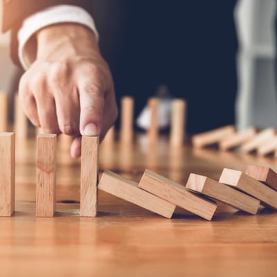 Hand holding up wooden domino preventing it form being knocked over by other dominos